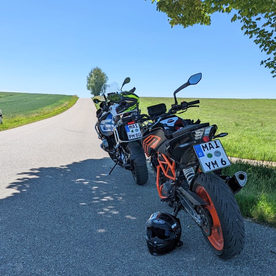 Zwei Motorräder parken am Rand einer asphaltierten, hügeligen Landstraße.