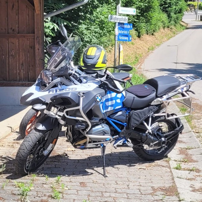 Weiße BMW R 1200 GS Adventure steht auf einem gepflasterten Weg, mit gelb-schwarzem Helm auf dem Tank.
