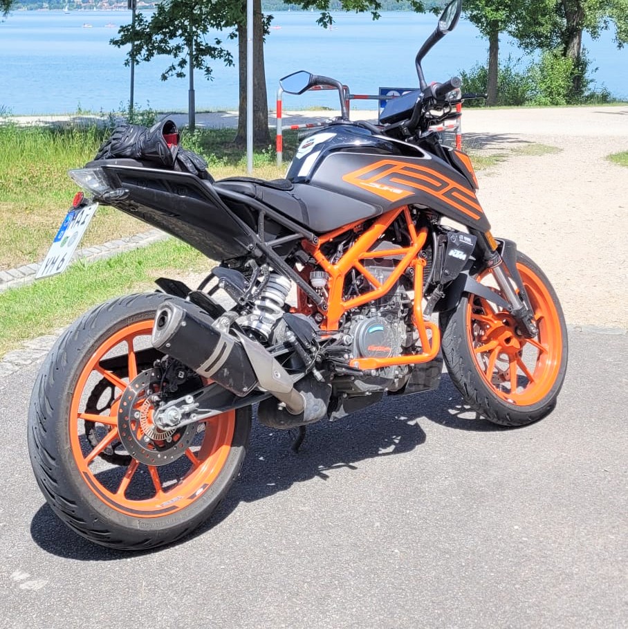 Grau-orangefarbenes KTM Duke Motorrad mit schwarzem Rahmen und orangefarbenen Felgen, frontal auf einem asphaltierten Weg.