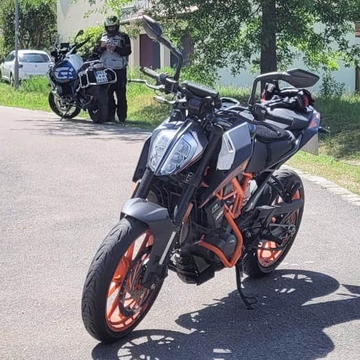 Grau-orangefarbenes KTM Duke Motorrad, mit schwarzem Rahmen und orangefarbenen Felgen, steht auf einem asphaltierten Weg.