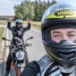 Zwei Motorradfahrer auf einer Landstraße; einer im Vordergrund mit Shoei-Helm, einer im Hintergrund auf einer KTM.