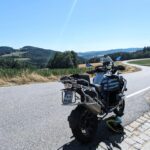 Heckansicht einer blau-silbernen BMW R 1200 GS an einer Landstraße in hügeliger Landschaft.