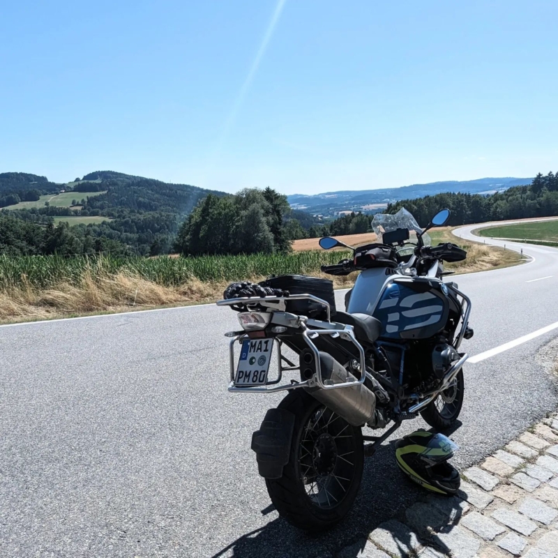 2023-07-15_1 Heckansicht einer blau-silbernen BMW R 1200 GS an einer Landstraße in hügeliger Landschaft.