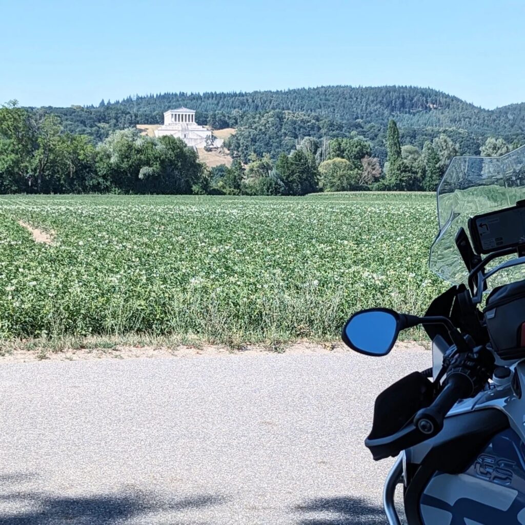 Blick über ein grünes Feld auf die Walhalla bei Regensburg, im Vordergrund der Lenker einer blau-silbernen BMW R 1200 GS.