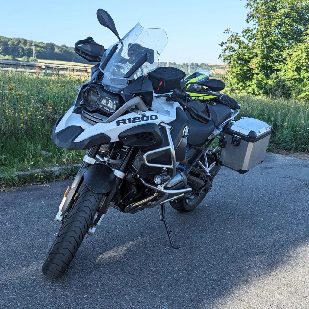 Weiß-schwarze BMW R1200 GS Adventure mit Alu-Koffern, Sturzbügeln und Tankrucksack parkt auf einer Landstraße.