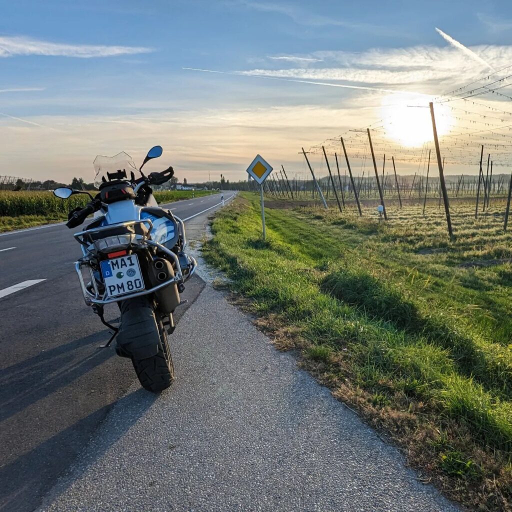BMW Motorrad parkt am Straßenrand neben Hopfenfeldern bei tiefstehender Sonne.