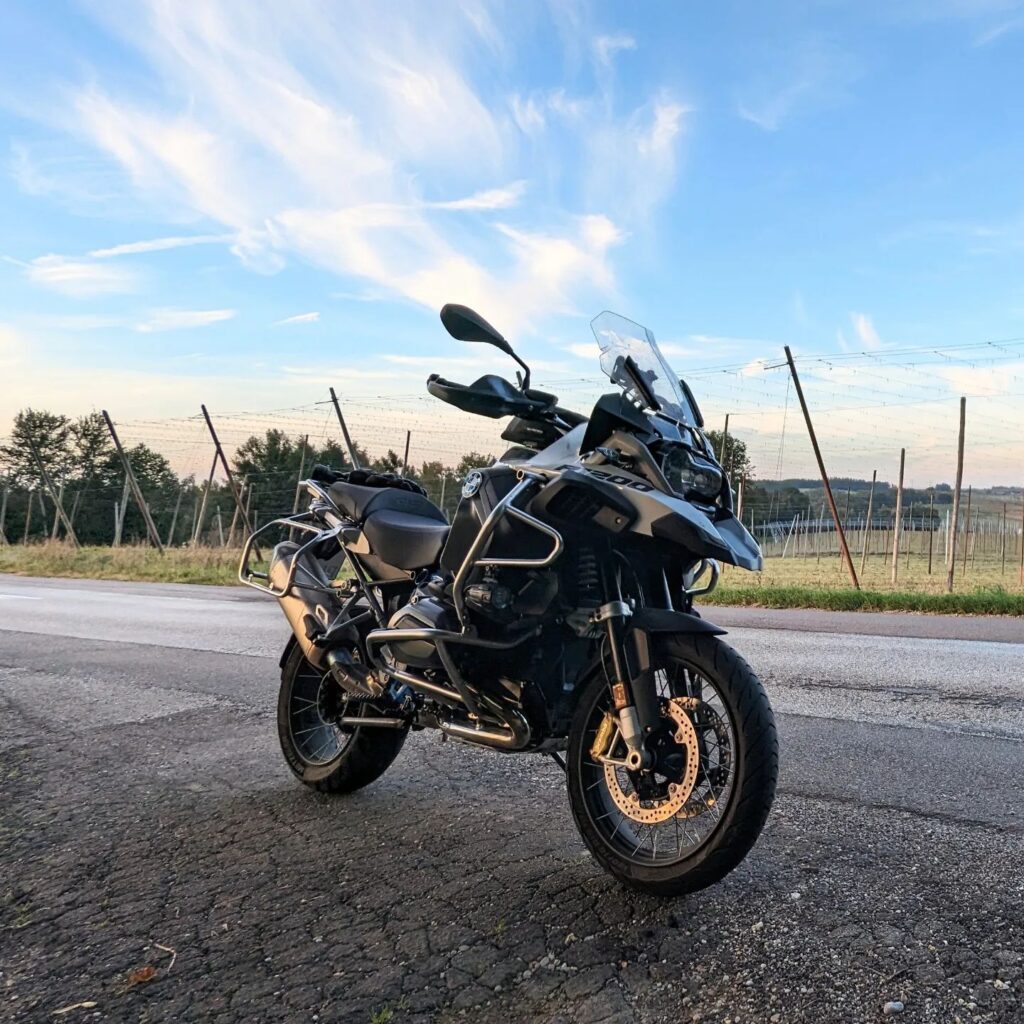 BMW R 1200 GS Adventure mit Sturzbügeln auf Asphalt vor einem Hopfenfeld bei Sonnenuntergang.