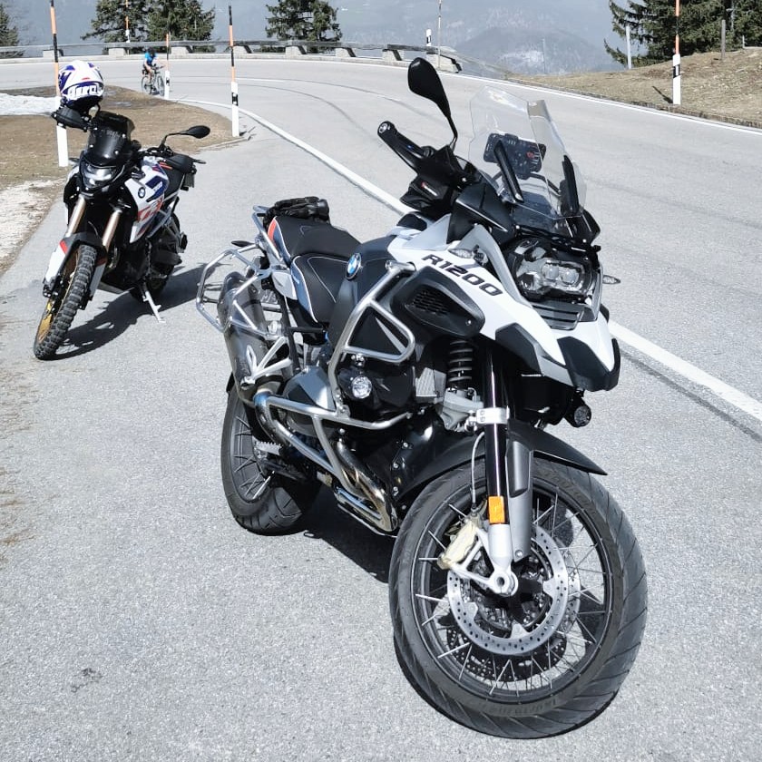 Zwei Motorräder, vorne eine weiße BMW R 1200 GS, auf einer asphaltierten Bergstraße an einem sonnigen Tag.