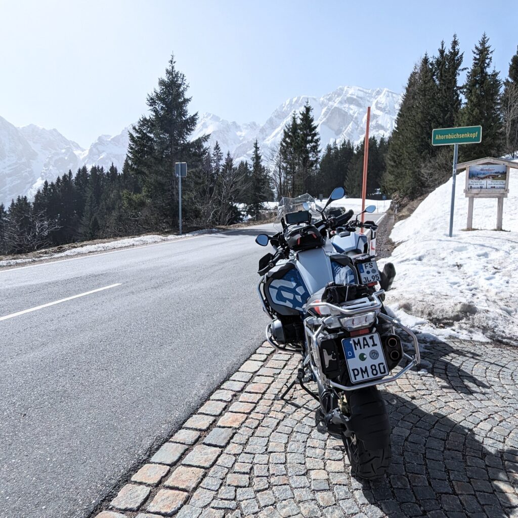 BMW R 1200 GS Motorrad (grau/weiß) parkt auf Kopfsteinpflaster am Straßenrand mit Schild "Ahornbüchsenkopf".