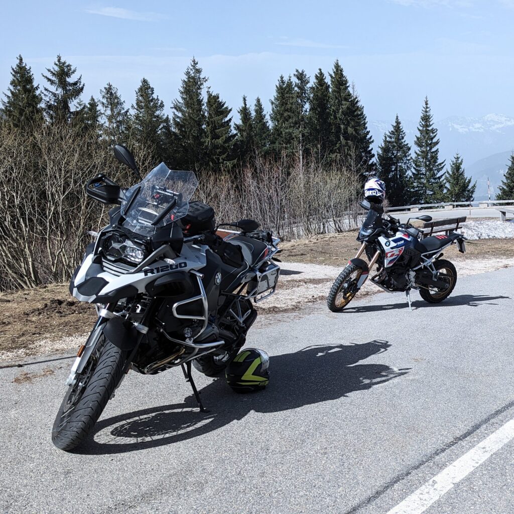 Zwei Motorräder parken am Straßenrand, eine graue BMW R 1200 GS im Vordergrund und ein gelber Helm auf dem Asphalt.