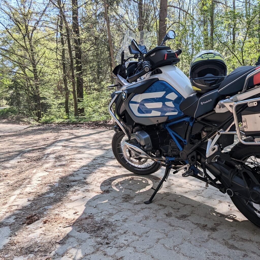 Weiße und blaue BMW R 1200 GS Adventure (Enduro-Motorrad) mit gelbem Shoei Helm auf einem Waldweg im Sonnenschein.