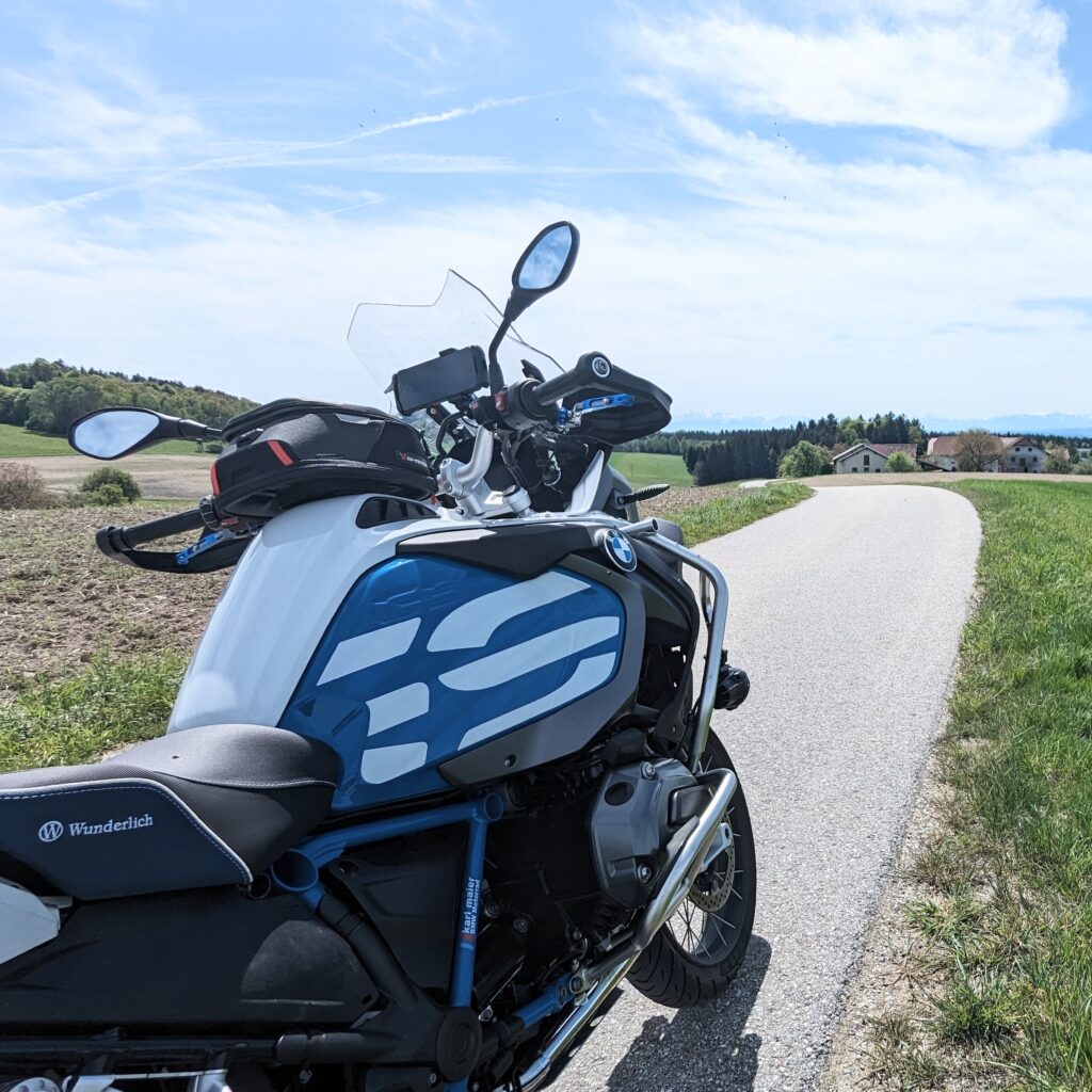 Ein weiß-blaues BMW R 1200 GS Adventure Motorrad auf einer asphaltierten Landstraße in hügeliger Landschaft. Wunderlich-Sitzbank.