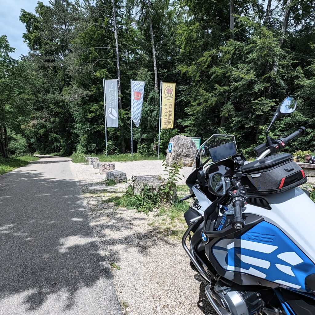 Motorrad (weiße BMW R 1200 GS) auf einem Feldweg neben drei Bannern mit "Naturpark Altmühltal" und dem bayerischen Rautenmuster.