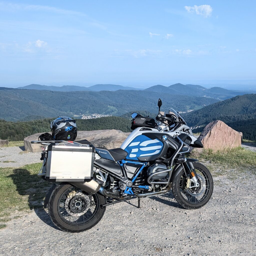 BMW R 1200 GS Adventure Motorrad in Blau/Weiß mit Aluminium-Seitenkoffern auf einem Aussichtspunkt in den Bergen.