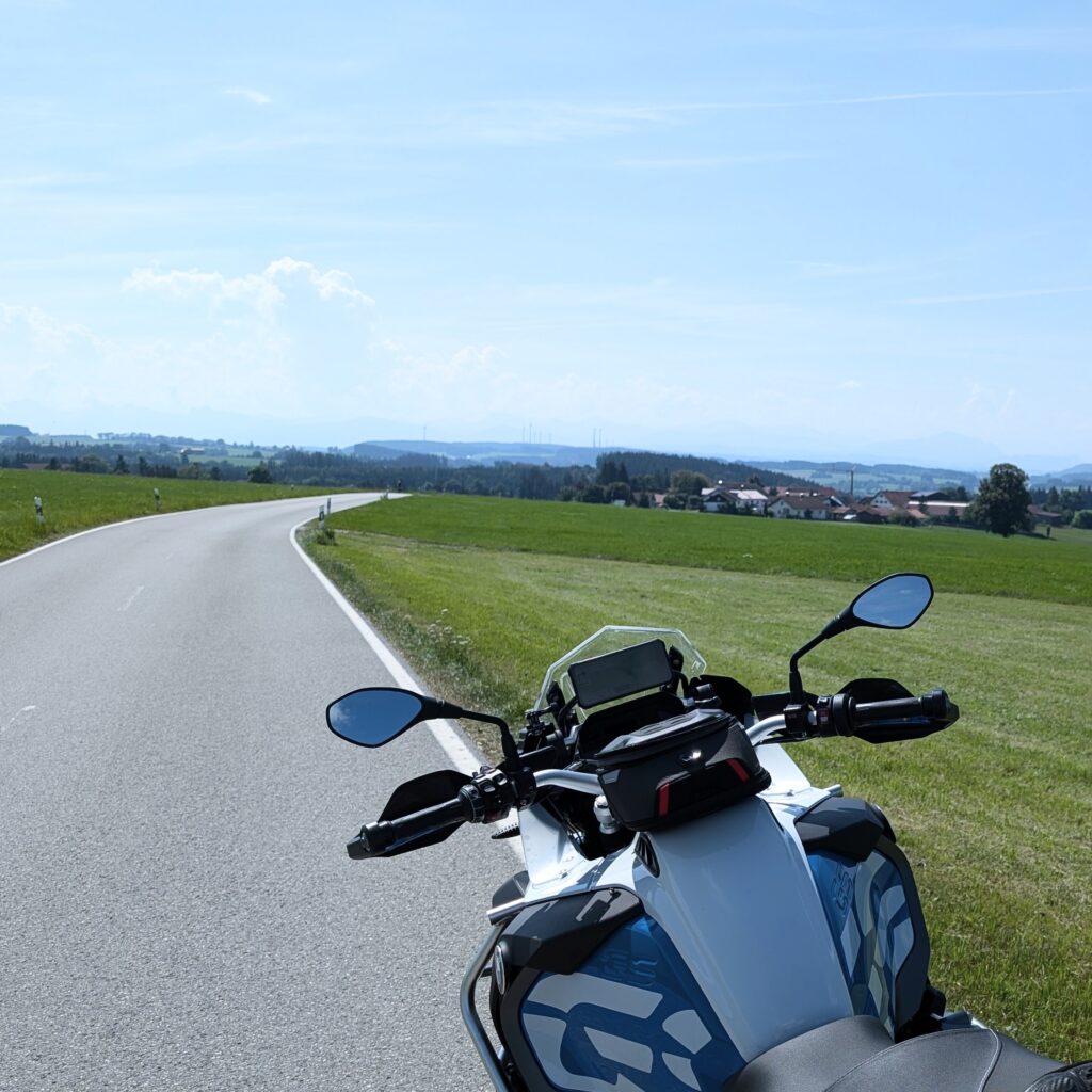 Eine BMW R 1200 GS Adventure mit Tanktasche steht an einer kurvigen Landstraße in grüner, hügeliger Landschaft.