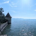 Historischer, runder Seeturm mit dunklem Dach am Bodensee mit glitzerndem Wasser und weiter Sicht.