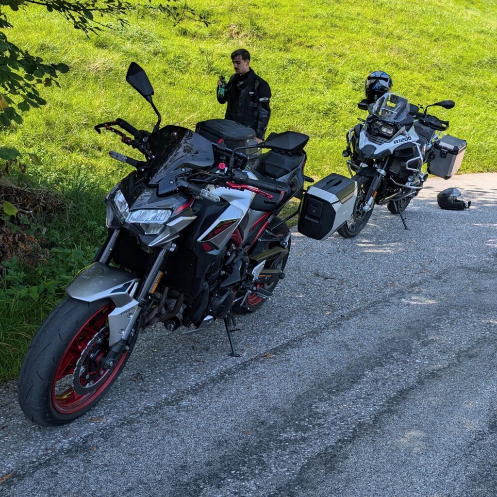 Eine silber-schwarze Kawasaki Z900 und eine BMW R1200 GS stehen am Straßenrand. Im Hintergrund ein Fahrer.