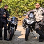 Zwei Motorradfahrer in voller Schutzkleidung stehen neben ihren Maschinen: einem Naked Bike und einer BMW Adventure.