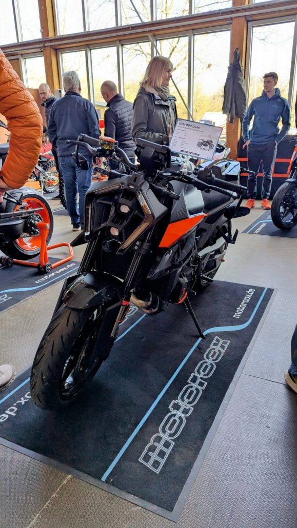 Schwarze KTM 890 Duke mit orangefarbenen Akzenten, auf einer Messe auf einem schwarzen Teppich mit "motorbox.de"-Logo.
