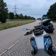 Motorrad (BMW R1200 GS) auf einem Kopfsteinpflasterstreifen am Straßenrand einer Autobahn und Strommast im Hintergrund.
