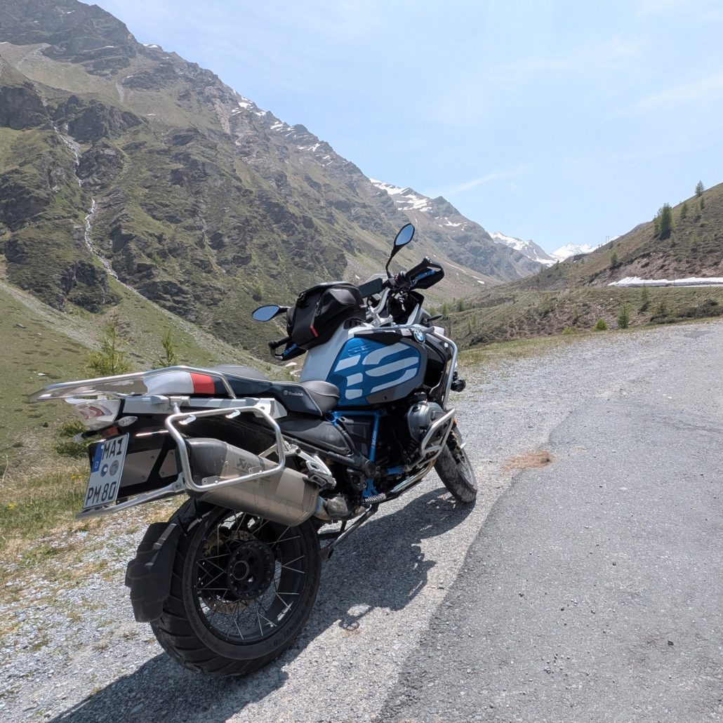BMW R 1200 GS Adventure Motorrad in Silber und Blau mit Gepäckträgern am Straßenrand in alpiner Berglandschaft mit Schnee.