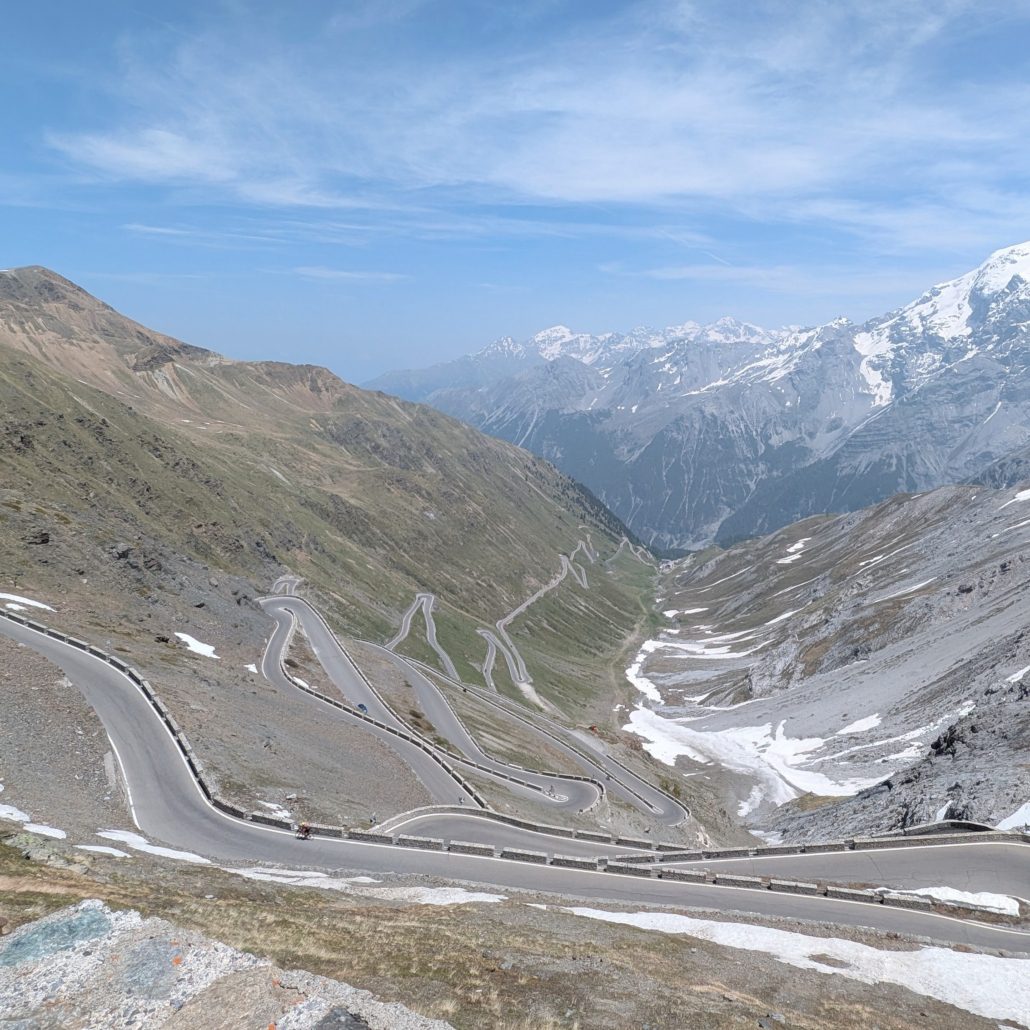 Panoramablick auf die Serpentinen der Stilfser-Joch-Straße, umgeben von schneebedeckten und felsigen Berggipfeln der Alpen.