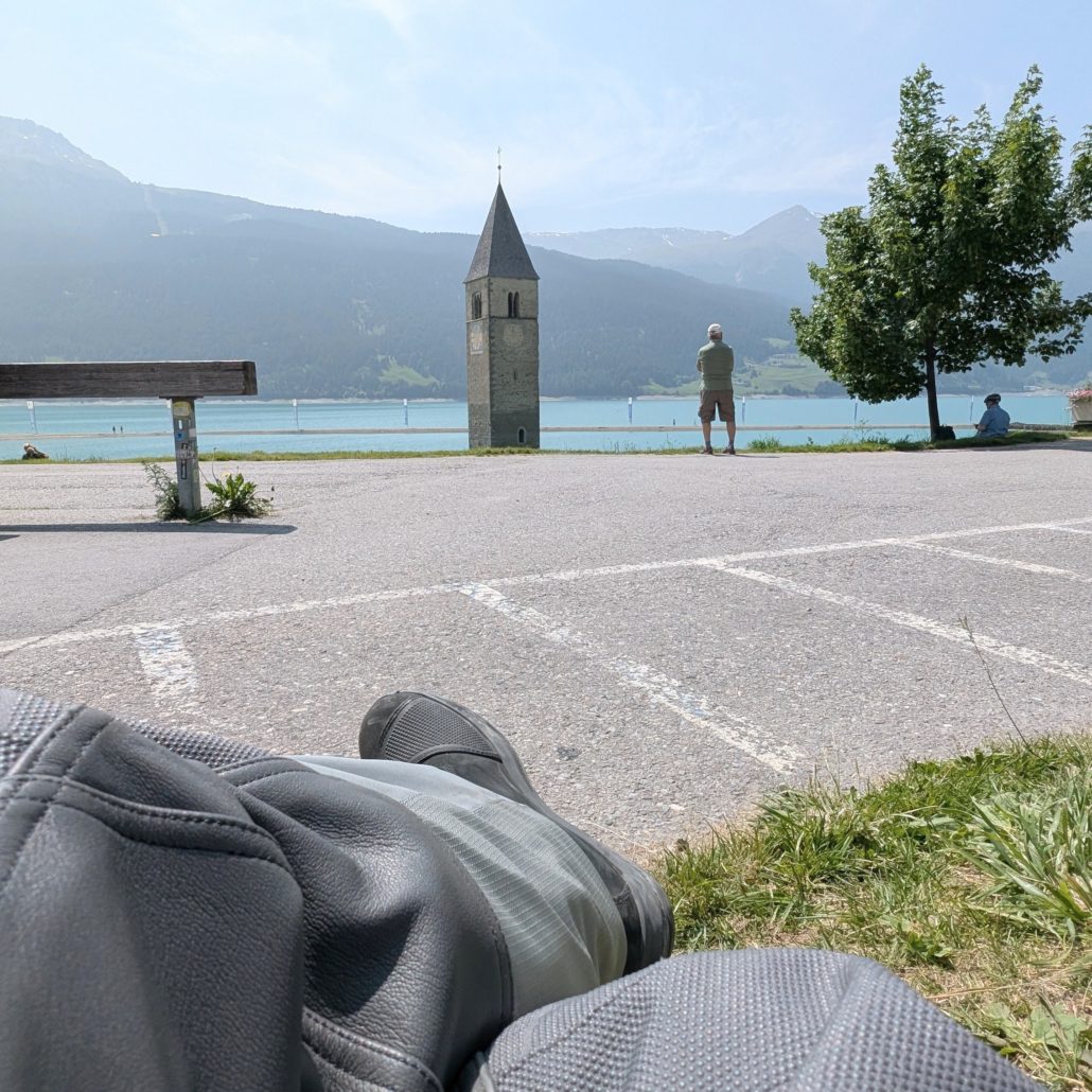 Unterwasser-Kirchturm von Graun im Reschensee in Südtirol, gesehen aus der Perspektive einer Motorradfahrers.