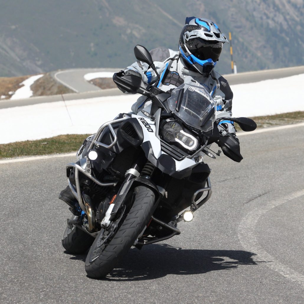 Motorradfahrer in grauer und blauer Schutzkleidung fährt eine weiße BMW R 1200 GS Adventure in einer scharfen Bergkurve.