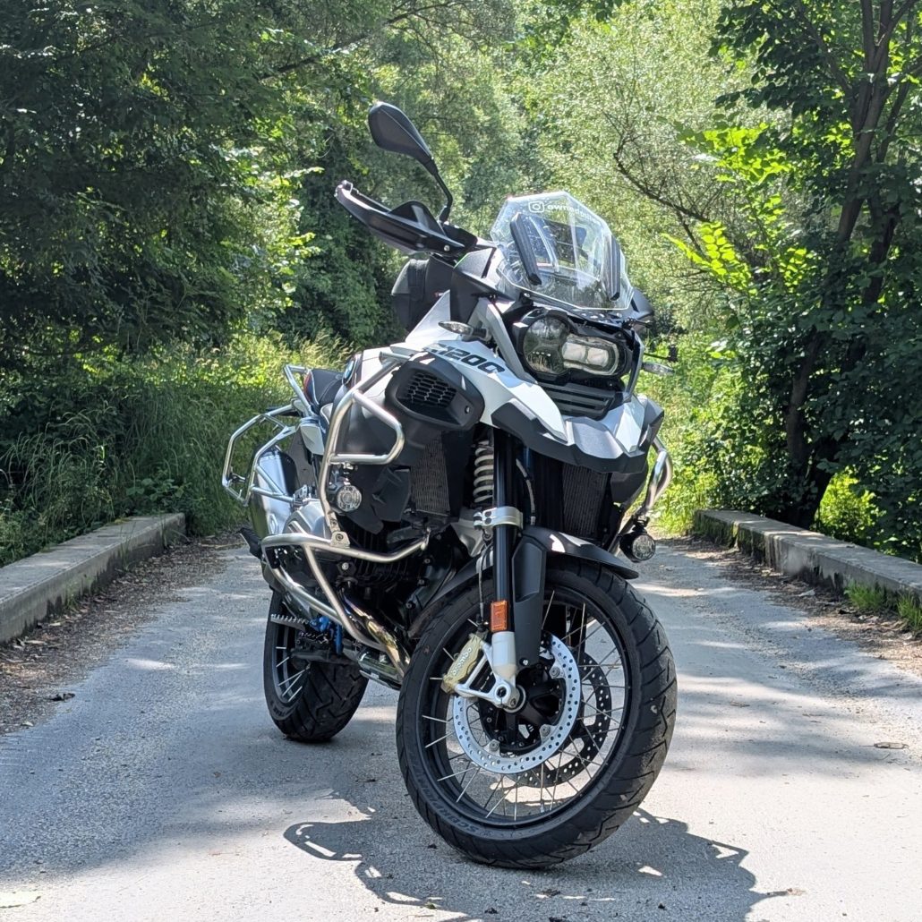 Motorrad auf Brücke in waldiger Umgebung, frontal aufgenommen. Schwarze und weiße Karosserie, silberne Sturzbügel.