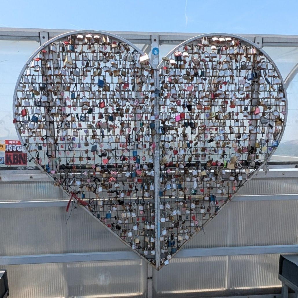 Herzförmiges Drahtgitter gefüllt mit vielen bunten Liebesschlössern auf einer Aussichtsplattform.
