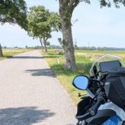 2025-06-18_14 Motorrad auf einer Landstraße mit Baumreihe und Windrädern im Hintergrund.