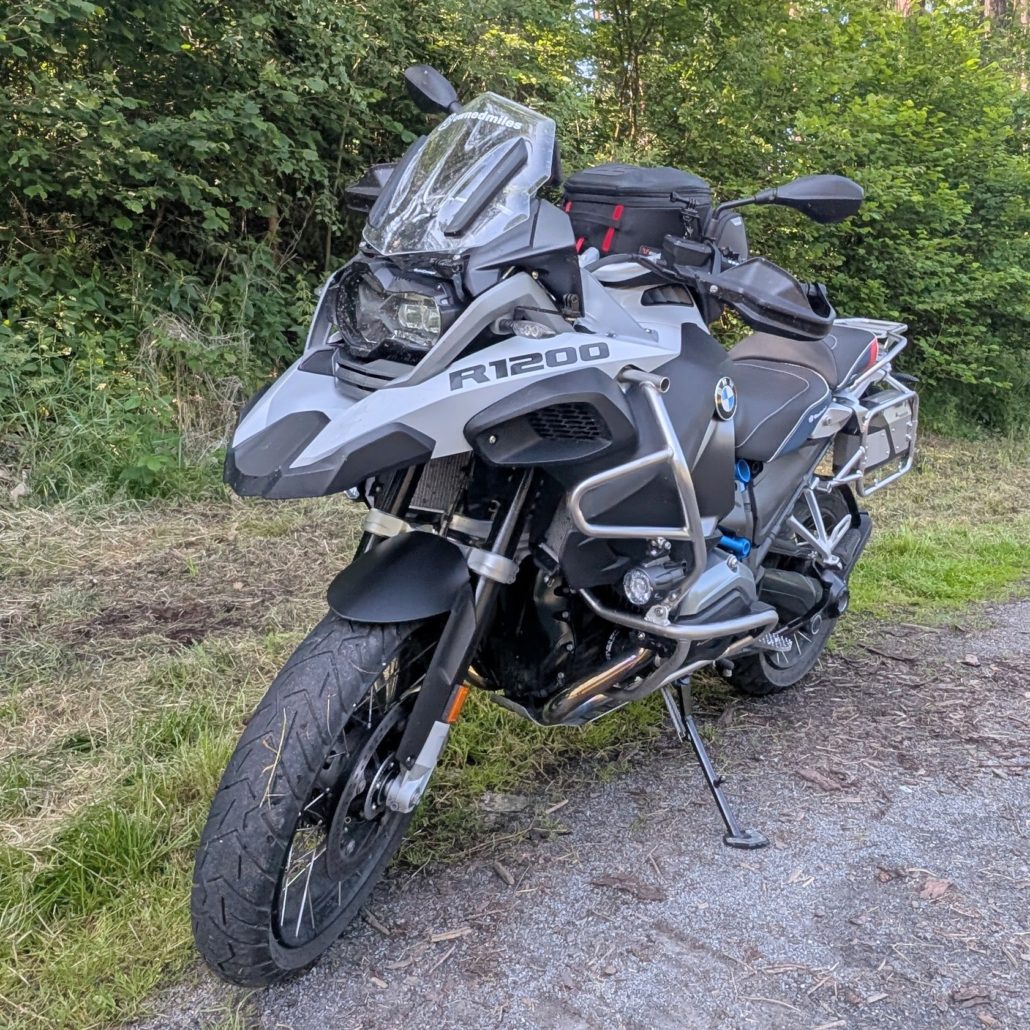 BMW R 1200 GS Motorrad in Grau/Schwarz mit blauen Akzenten, steht in bergiger Landschaft bei Sonnenschein.