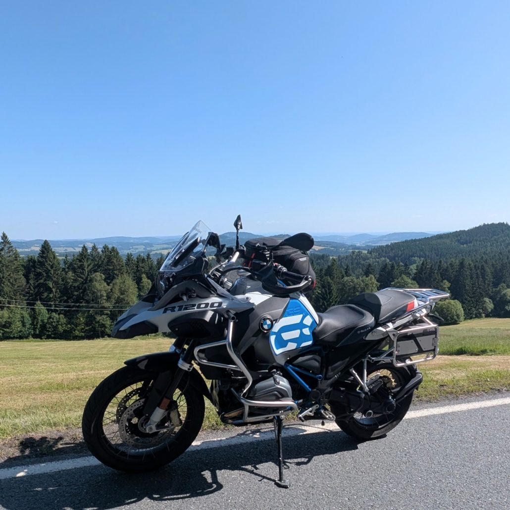 Graue BMW R 1200 GS Adventure steht am Straßenrand mit Blick auf bewaldete Hügel und eine weite Landschaft.