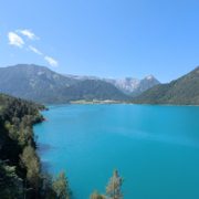 Türkisblauer Achensee in Tirol, umgeben von dicht bewaldeten Bergen und einem kleinen Dorf am Ufer unter klarem Himmel.