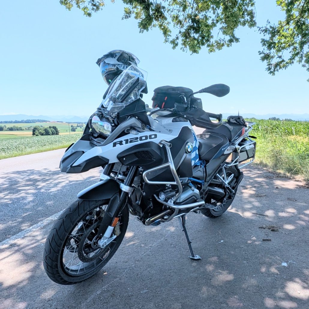 BMW R1200 GS Adventure Motorrad in Weiß-Schwarz auf einem Seitenständer am Straßenrand unter einem Baum.