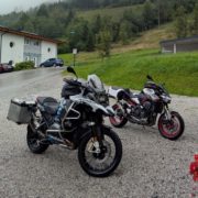 Zwei Motorräder parken auf einem Schotterparkplatz vor einem Haus: eine schwarze BMW R 1200 GS und eine Kawasaki Z900.