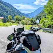 Motorrad mit Tankrucksack und Navigationsgerät, geparkt an einer Bergstraße vor einem sonnigen, grünen Tal.