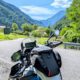 Motorrad mit Tankrucksack und Navigationsgerät, geparkt an einer Bergstraße vor einem sonnigen, grünen Tal.