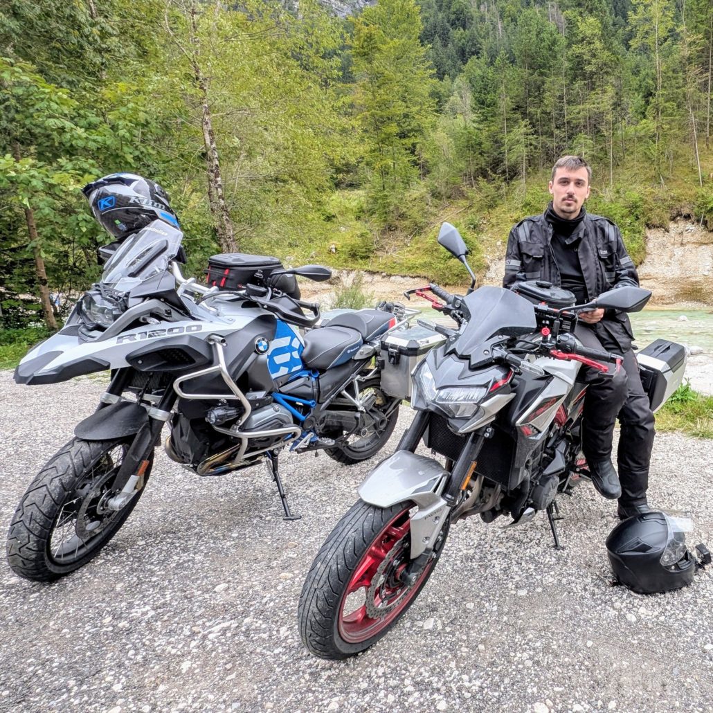 Mann in schwarzer Motorradkleidung sitzt auf einem grauen Naked Bike (Kawasaki Z) neben einer BMW GS Adventure auf Schotter.