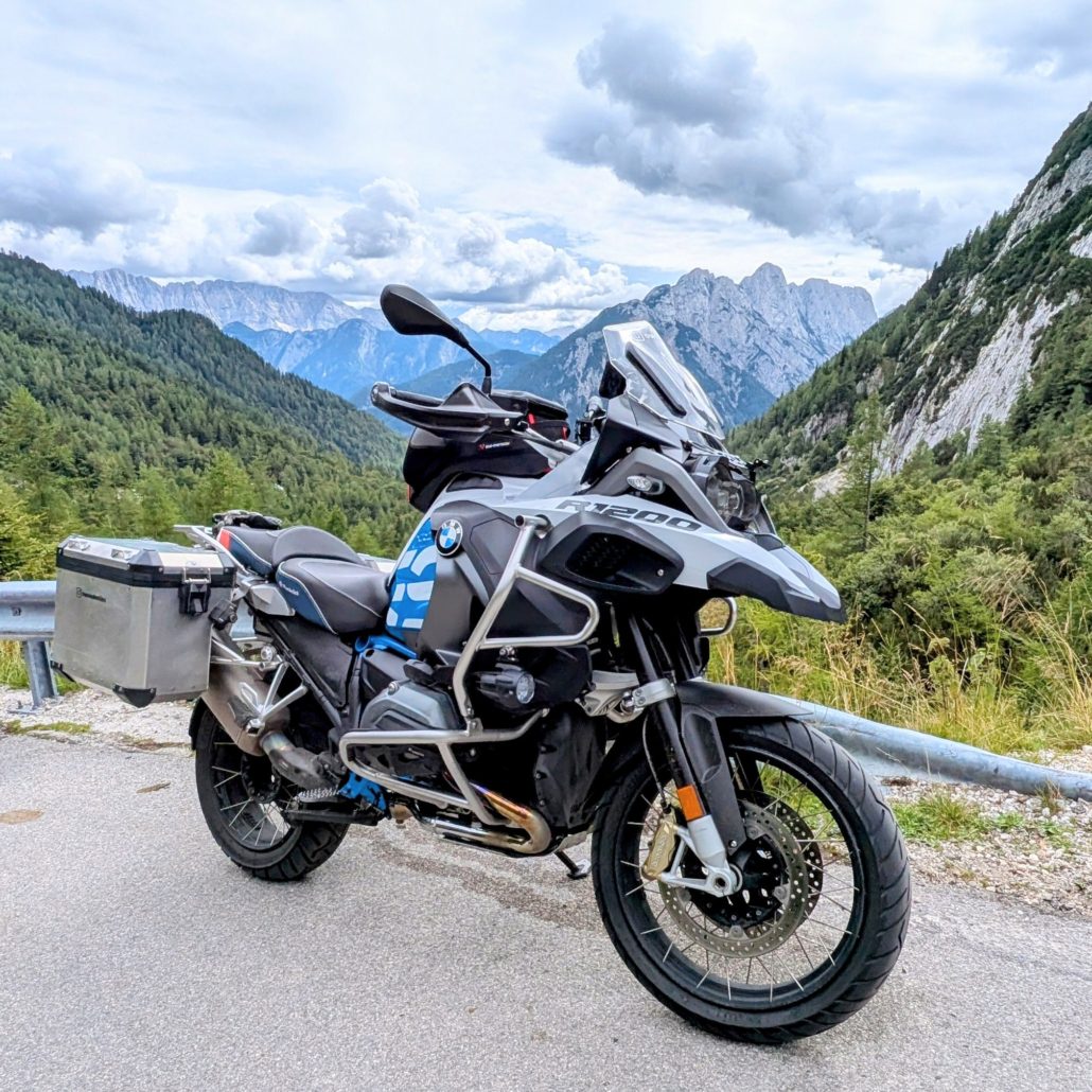 Weiße und blaue BMW R1200 GS Adventure mit silbernen Koffern und Sturzbügeln auf einer Bergstraße in den Alpen.