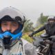 Selfie von zwei Motorradfahrern in Helmen, der Vorderste trägt einen graublauen Helm, im Hintergrund nebelige Berge.