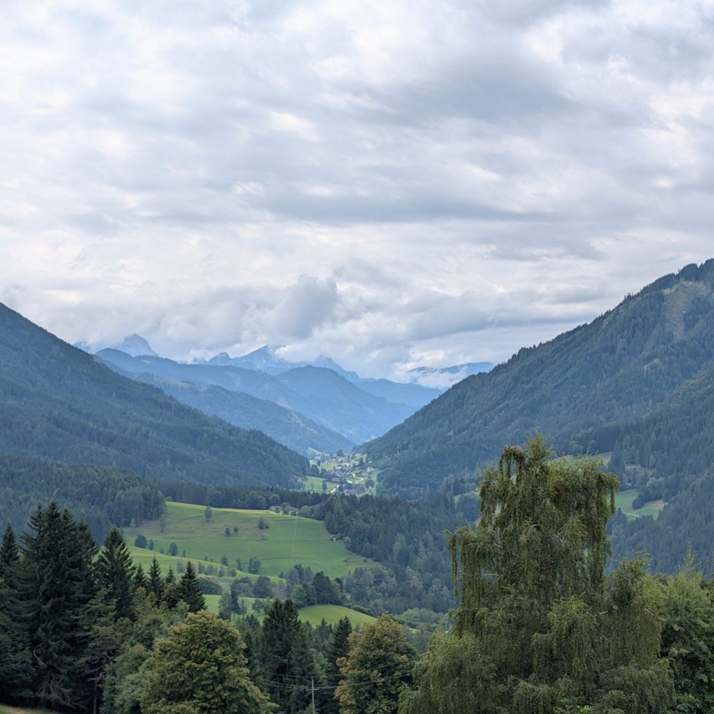 Motorrad-Tagesausflug: Blick auf ein grünes, waldreiches Bergtal mit kleinen Dörfern unter einem bewölkten Himmel.