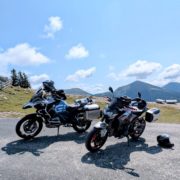 Zwei Motorräder (BMW GS und Kawasaki Z900) parken an einer Passstraße vor einer Bergkulisse.