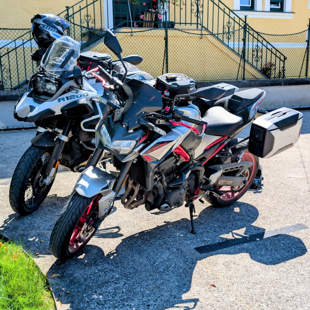 Silberne Kawasaki Z900 mit rotem Rahmen und Koffern neben einer weißen BMW R1200 Reiseenduro geparkt.