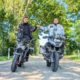 Zwei Motorradfahrer auf Naked Bike und BMW R1200 GS beim Faustgruß auf einer sonnigen Allee.