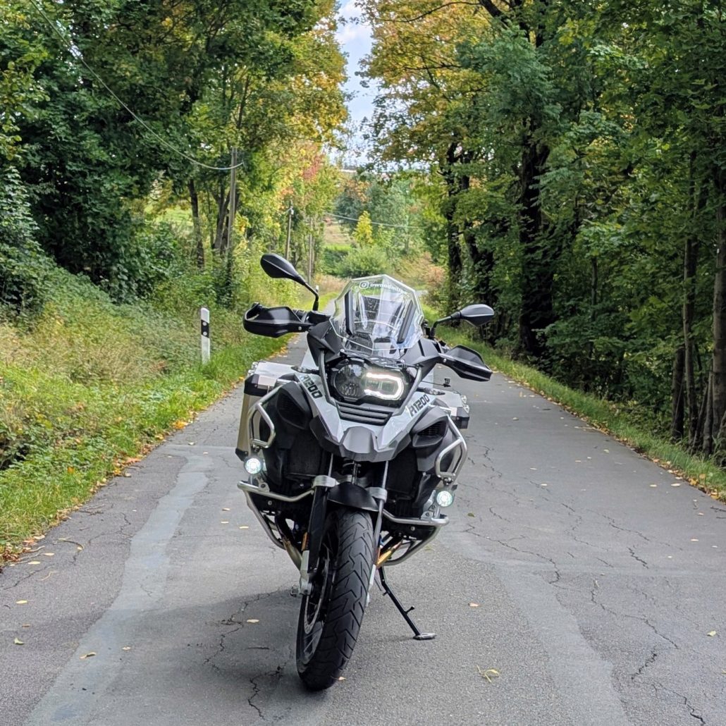 BMW R 1200 GS Adventure auf schmaler, von Bäumen gesäumter Waldstraße, gesehen von vorne.