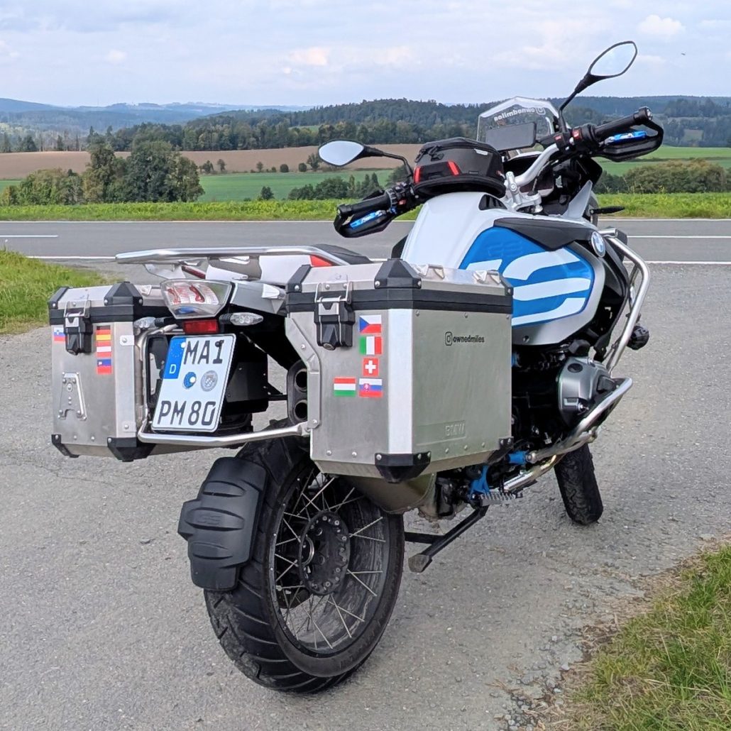 Sicht vom Lenker einer BMW R 1200 GS auf eine schmale, von Bäumen gesäumte Straße im Herbst.