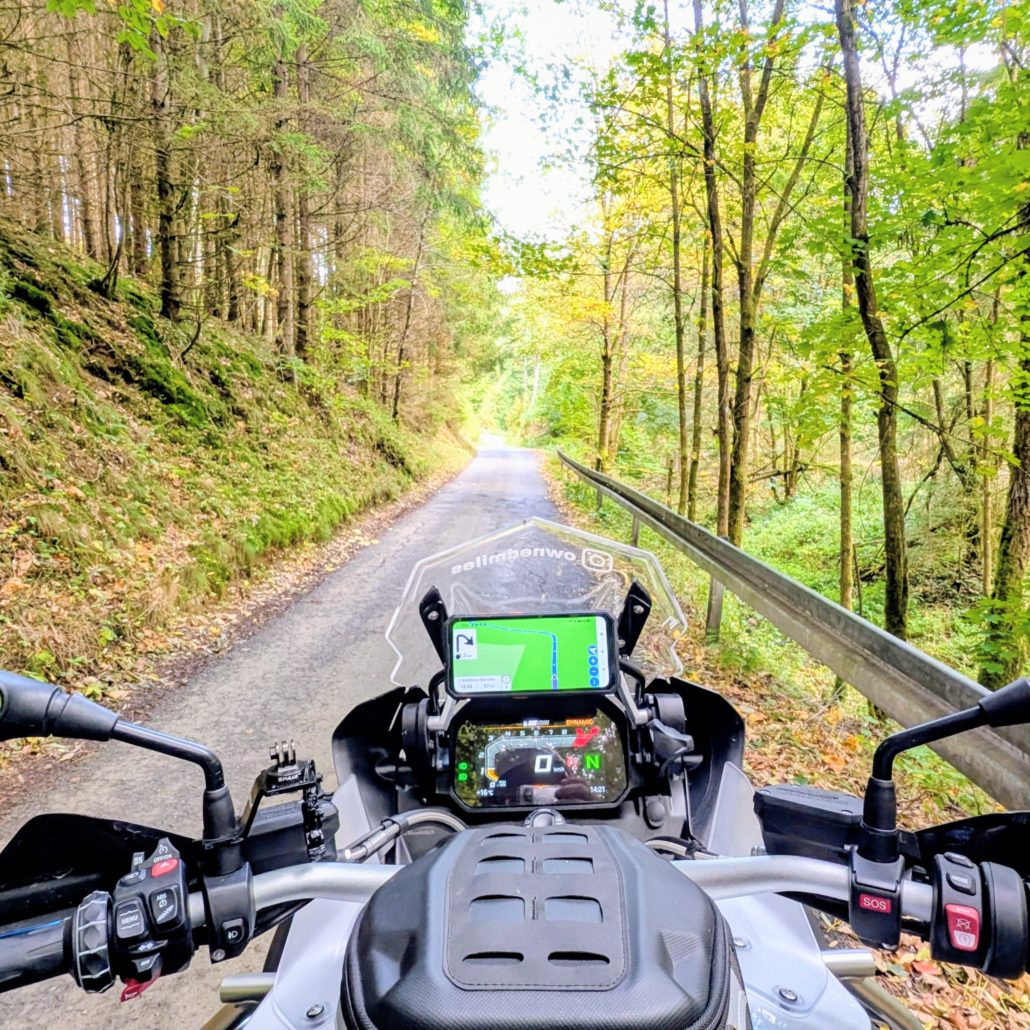 Grau-schwarze BMW R 1200 GS Adventure mit silbernem Koffer parkt am Straßenrand vor herbstlicher Waldkulisse.