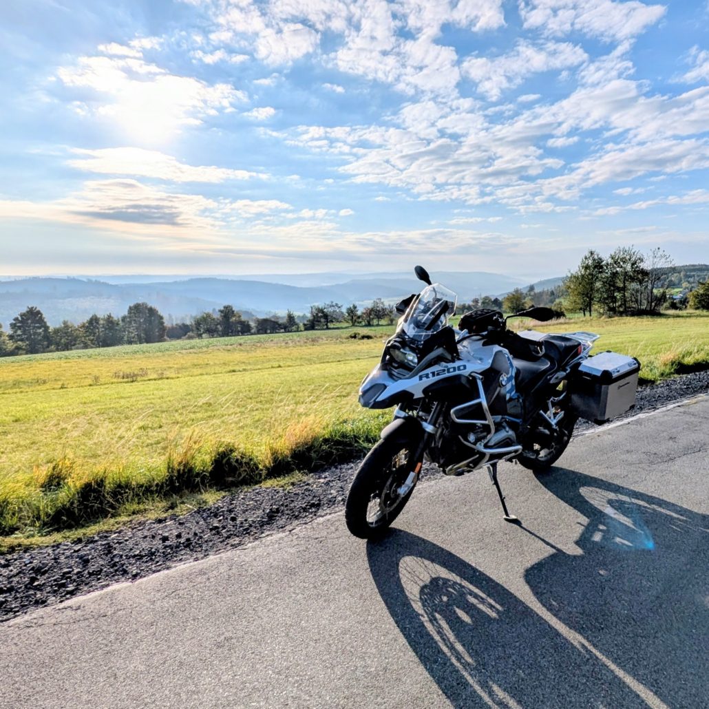 Weiße BMW R 1200 GS Adventure mit Seitenkoffern, geparkt an einer Landstraße mit weitem Blick über hügelige Landschaft.