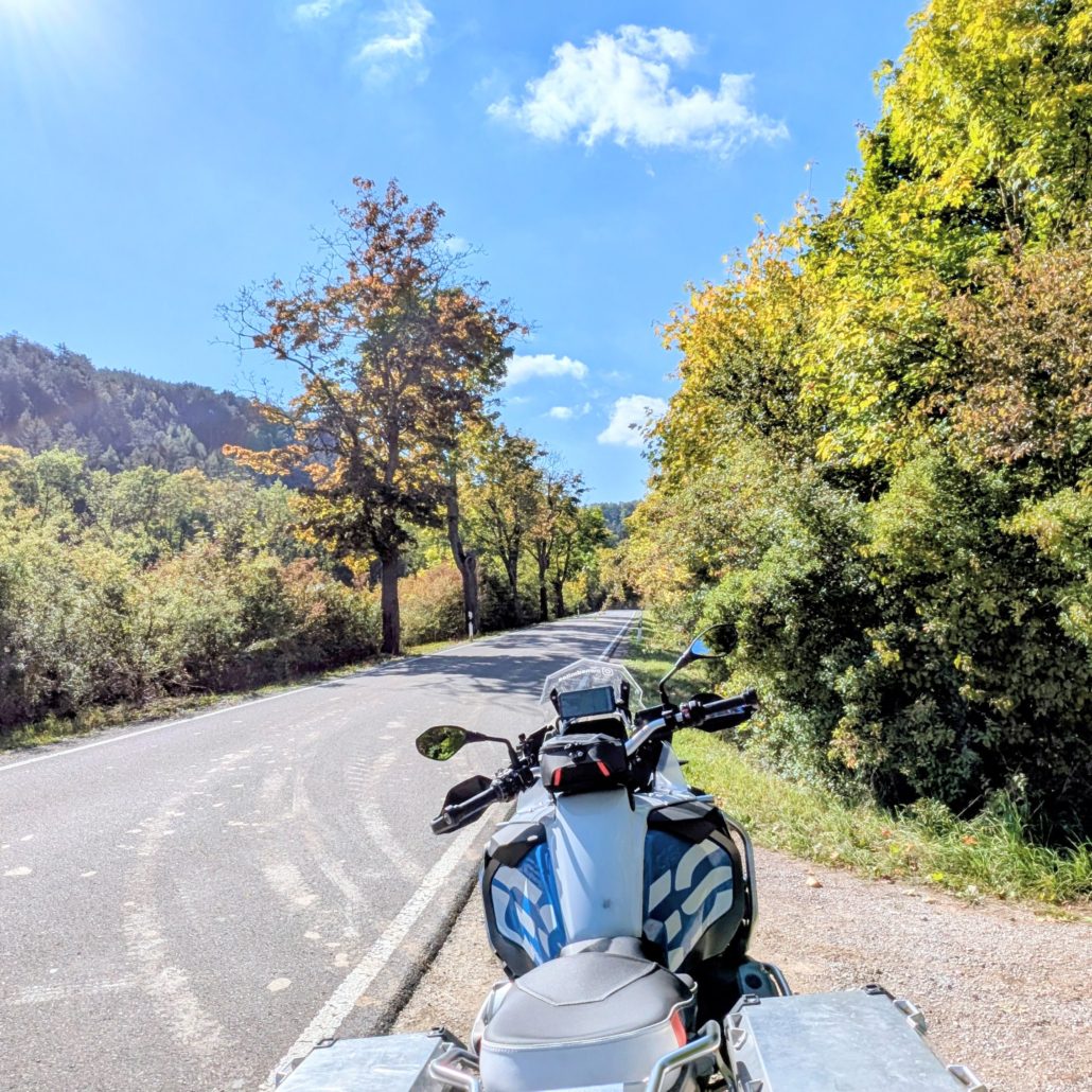 Motorrad auf einer ländlichen Straße im Herbst; der Himmel ist blau mit weißen Wolken.
